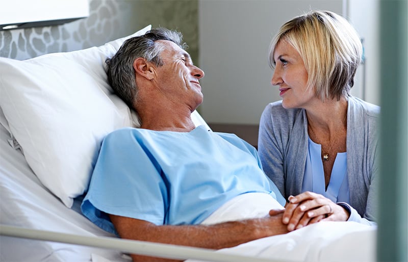 A patient smiling with a loved one who is standing next to the hospital bed